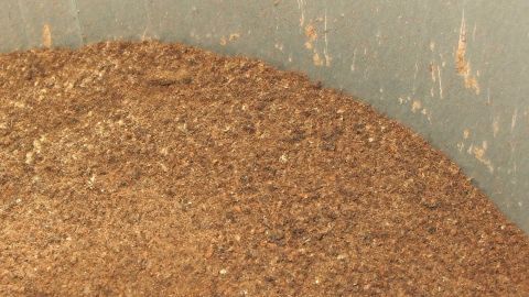 Kupfer mit Holzasche wird in einem Behälter vermischt, um das Kupfer zu reinigen. Die Asche hat eine goldbraune Farbe.