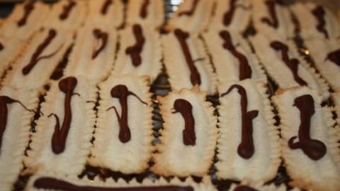 Zarte Spritzgebäck nach Omas Art liegt in Reihen, mit schokoladiger Glasur dekoriert, auf einem Blech zum Abkühlen.