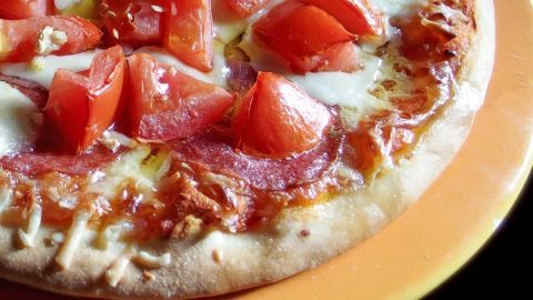 Ein Pizza mit frischen Tomatenstücken und Käse liegt auf einem orangefarbenen Teller, bereit zum Genießen.