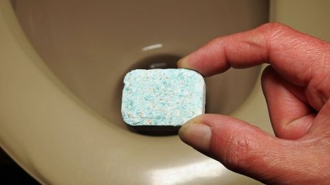 Ein Geschirrspülreiniger wird mit einer Hand in eine Toilette gehalten, um Ablagerungen zu entfernen.