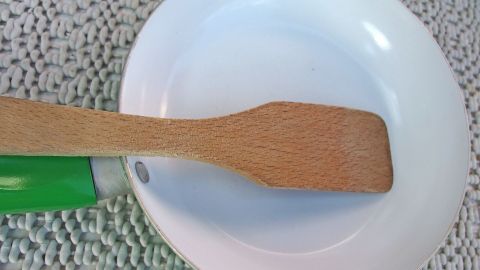 Ein Holzschaber liegt auf einem weißen Teller, bereit, um Angebranntes zu lösen, auf einem strukturierten Untergrund.