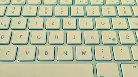 Eine weiße PC-Tastatur mit deutschen Buchstabentasten wird aus der Vogelperspektive gezeigt, umrahmt von einem dunklen Hintergrund.