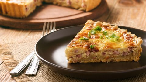 Ein Stück Kasseler Speckkuchen liegt auf einem dunklen Teller, frisch serviert auf einem rustikalen Tisch mit Holzmaserung.