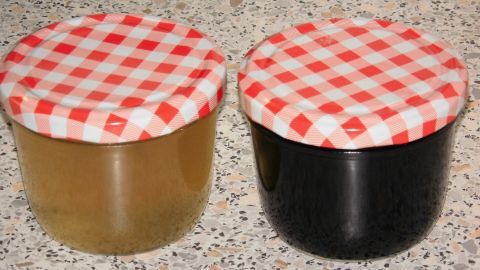 Zwei Gläser mit Weingelee, eines hell und eines dunkel, stehen auf einer marmorierten Oberfläche mit rot-weißem Deckel.