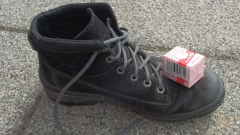 Ein schwarzer Schuh steht auf dem Boden, während ein Päckchen Hefe oben darauf platziert ist, um Fußpilz zu behandeln.