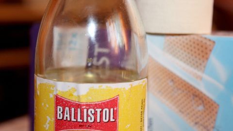Eine Flasche Ballistol steht neben einem Verband und einer Packung mit Pflastern, bereit zur Behandlung von Wunden und Pickeln.