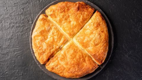 Ein goldbrauner Kartoffelkuchen liegt auf einer dunklen Platte, in vier gleichmäßige Stücke geschnitten.