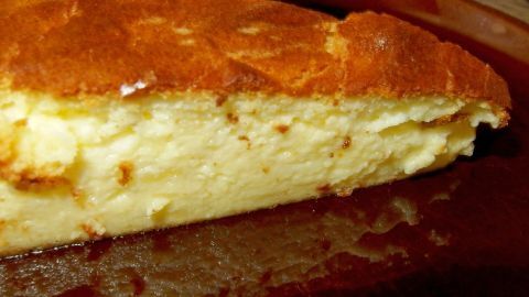 Ein Käsekuchen ohne Boden liegt auf einem Teller und zeigt eine goldbraune, leicht gebräunte Oberfläche, umgeben von einem schlichten Hintergrund.