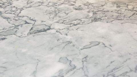 Eine glänzende Marmoroberfläche zeigt leichte Säureschäden, die auf eine bevorstehende Reparatur mit Nassschleifpapier hinweisen.