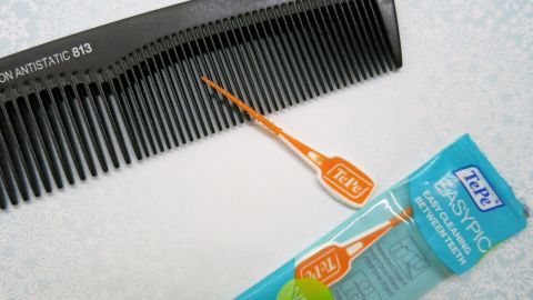 Ein schwarzer Kamm wird mit einem orangen TePe EasyPick gereinigt. Der Hintergrund ist eine helle, gemusterte Fläche.