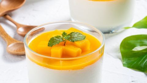 Gläser mit cremiger Fruchtsauce und frischen Mangowürfeln, dekoriert mit Minze, auf einem weißen Tisch.
