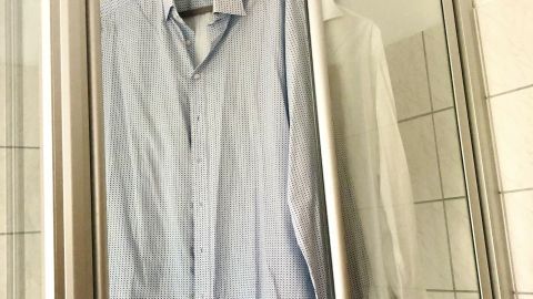 Im Badezimmer hängen ein blauer Hemd und ein weißes Hemd zum Trocknen an einer Stange in einer Dusche.