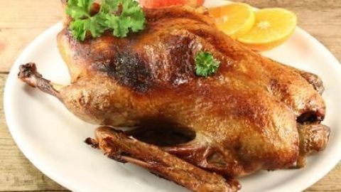 Bratente liegt einladend auf weißem Teller, garniert mit Petersilie, umgeben von Orangen- und Apfelscheiben auf Holztisch.