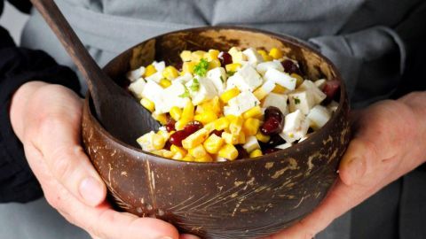 Ein Schüssel voller Partysalat mit Bohnen, Mais und Feta wird von einer Person gehalten und wirkt appetitlich und frisch.