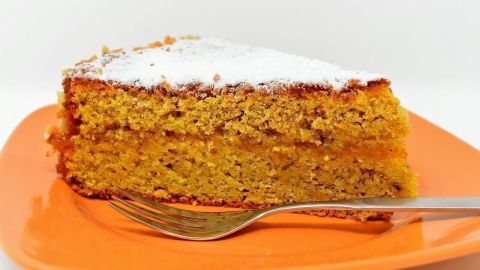 Ein Stück Karottenkuchen mit Nüssen liegt auf einem orangefarbenen Teller, bereit zum Servieren und Genießen.