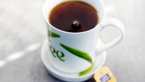 Mithilfe von schwarzem Tee lassen sich so manche Möbelstücke wieder auffrischen. Ein raffinierter Becher mit Tee steht auf einer Untertasse, während ein Teebeutel daneben liegt und die Lichtsituation entspannend wirkt.