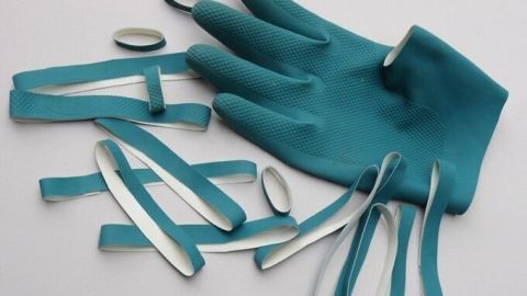 Ein abgenutzter, blauer Gummihandschuh liegt mit zerrissenen Gummiüberresten auf einer weißen Fläche, bereit zur Wiederverwertung.