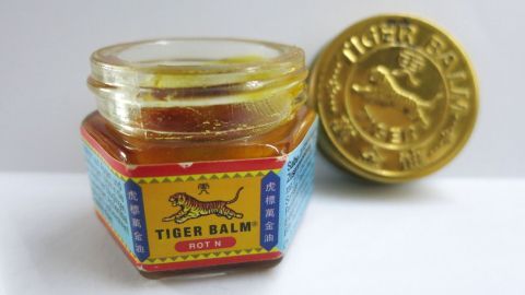 Ein Glas Tigerbalm Rot steht auf einem Tisch, daneben liegt eine goldene Münze, die den Kontext symbolisiert.