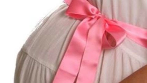 Ein schwangere Frau hält ihren Bauch, geschmückt mit einem rosa Band, das einen sanften, festlichen Eindruck vermittelt.