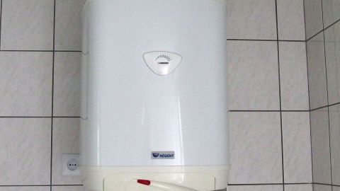 Ein elektrischer Durchlauferhitzer hängt an einer gefliesten Wand, bereit dazu, Wasser zu erwärmen und Energie zu sparen.