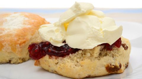 Ein scone liegt auf einem Teller, belegt mit Marmelade und einem großen Löffel Mascarpone, bereit zum Genießen.