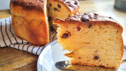 Ein frischer Panettone, bereits angeschnitten, liegt neben einer Gabel auf einem Teller, umgeben von einer gestreiften Serviette.
