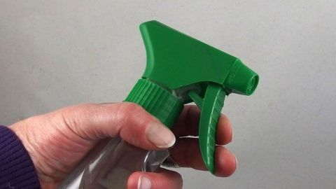 Leere Sprühflaschen muss man nicht wegschmeißen, man kann sie für verschiedene Zwecke weiterverwenden. Eine Hand hält eine grüne Sprühflasche, bereit zum Sprühen von Flüssigkeit in einem neutralen, hellen Hintergrund.