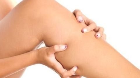 Eine Hand massiert eine Wade, was Wadenkrämpfe lindern kann. Der Hintergrund ist einfarbig weiß.