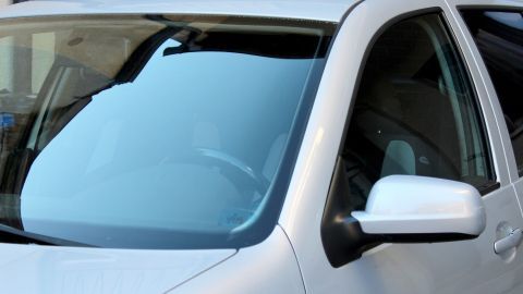 Ein silbernes Auto mit sauberer Windschutzscheibe steht vor einem modernen Gebäude ohne Baumharzflecken.