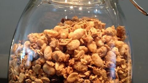 Glasbehälter mit Müsli, gefüllt bis zum Rand, steht auf einem Tisch in heller Umgebung.