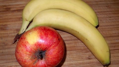 Rotäpfel und gelbe Bananen liegen auf einem Holzuntergrund, bereit zur Zubereitung einer fruchtigen Apfel-Bananen-Marmelade.