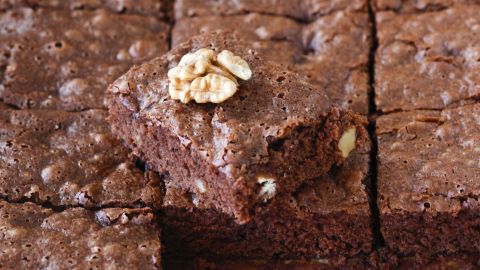 Saftige Nuss-Brownies liegen auf einem Tisch, eine Portion mit Walnüssen zeigt den köstlichen Schokoladenteig.