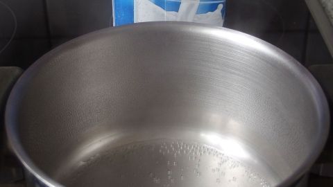 Ein silberner Kochtopf steht auf einem Herd, dampfend mit Wasser gefüllt, bereit zum Kochen von Milch.