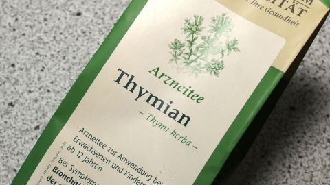 Eine Packung Thymiantee liegt auf einer grauen Fläche, betont die heilenden Eigenschaften gegen Husten.