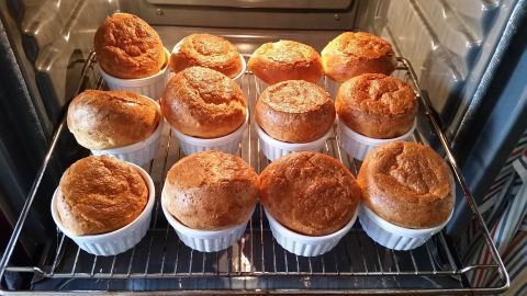 Im Ofen backen goldbraune Pfitzauf in weißen Förmchen, umgeben von anderen Leckereien auf einem Rost.