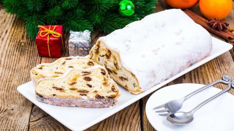 Ein geschnittenes Quarkstollen liegt auf einem Teller, umgeben von festlicher Deko und frischen Orangen.