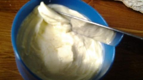 Ein blauer Schüssel mit kalt streichbarem Butter-Streichfett wird mit einem Messer glatt gestrichen, um Kräuterbutter zu zeigen.