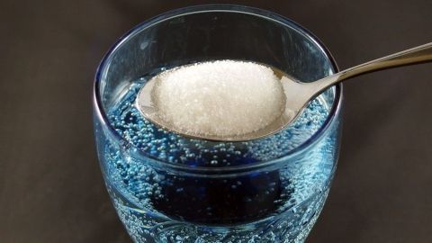 Ein Glas mit Zuckerwasser sprudelt, während ein Löffel mit Zucker darüber gehalten wird, um bei nächtlichem Husten zu helfen.