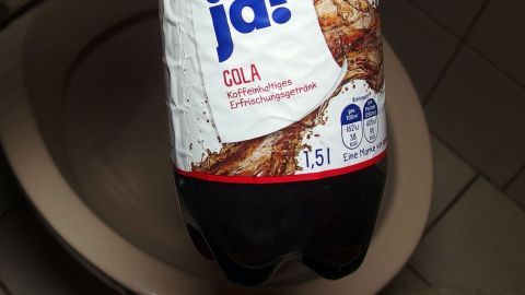 Bei ganz hartnäckigen Urinablagerungen hilf am besten Cola. Eine Cola-Flasche schwebt über einer Toilette, bereit zum Reinigen der WC-Schüssel mit dem Getränk.