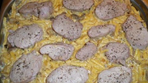 Schweinefilet-Scheiben liegen auf cremigen Spätzle in einer Metallform, umgeben von einer goldbraunen Käsesauce und Champignons.