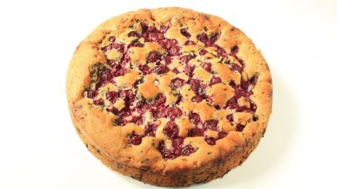 Ein runder Rührkuchen mit Kirschen bedeckt, liegt auf einem weißen Hintergrund und wartet darauf, serviert zu werden.