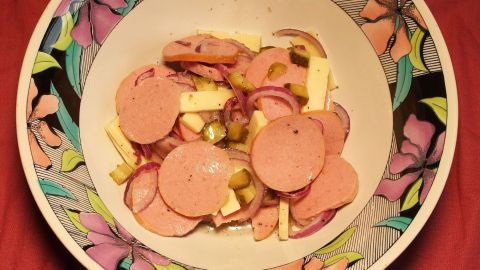 Ein bunter Wurst-Käse-Salat liegt in einer dekorativen Schüssel und zeigt geschnittene Wurst- und Käsestückchen mit Zwiebeln.