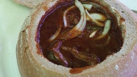Eine kreative Jägersuppe serviert in einem Brotteller, reich an Zwiebeln und gefüllt mit herzhaftem Eintopf.
