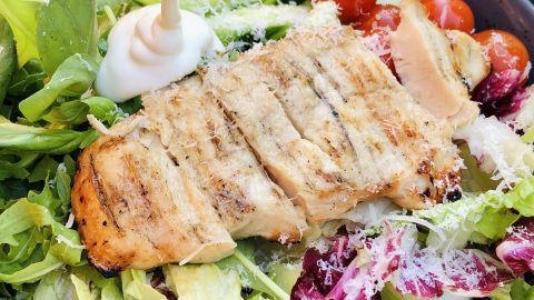 Ein bunter Salat mit gegrilltem Hähnchen wird mit cremiger Mayonnaise in einer Schale übergossen.
