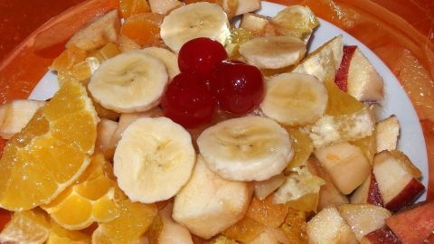 Bunter Obstsalat auf einem Teller, belegt mit Bananen, Äpfeln, Mandarinen und Kirschen, frisch zubereitet.