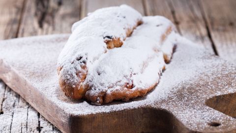 Ein Stollen, mit Puderzucker bestäubt, liegt auf einem Holzbrett und erwartet festliche Freude. Weihnachten und Quark sind präsent.