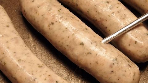 Gegrillte Bratwürste liegen auf einem Blech, während ein Thermometer zur Temperaturkontrolle eingesetzt wird.