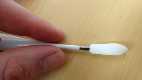 Kindern Fieberzäpfchen verabreichen: schnell, einfach und ohne große Quälerei, mithilfe eines Fieberthermometers. Ein Fieberzäpfchen wird mit der Hand gehalten und steht auf einer Holzoberfläche, bereit zur Anwendung bei Kindern.