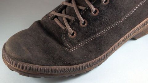 Ein brauner Wildlederschuh liegt auf einer hellen Oberfläche, er zeigt leichte Abnutzung und wartet auf Pflege mit Teppichschaum.