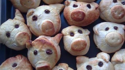 Glücksschweine aus Gebäck mit Rosinenaugen liegen nebeneinander auf einem Backblech.